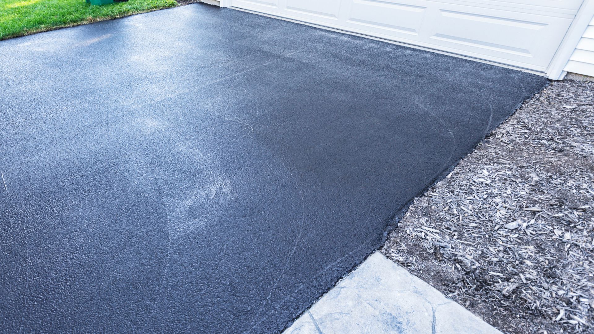 A driveway with a black tarmac and a white garage door